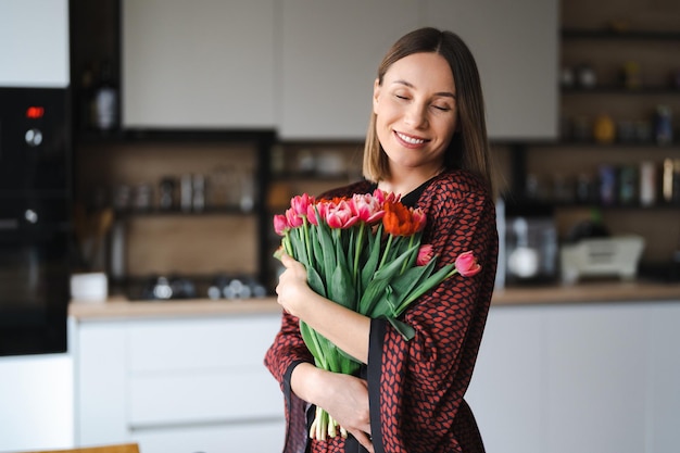 Mulher feliz desfruta de buquê de tulipas dona de casa desfrutando de um monte de flores e interior da cozinha doce lar sem alergia