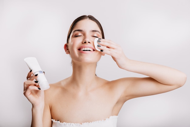 Mulher feliz desfrutando de spa facial. a modelo limpa o rosto com uma esponja antes de aplicar o creme.
