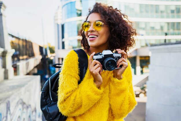 Mulher feliz e confiante segurando a câmera fotográfica e andando na grande cidade moderna. +