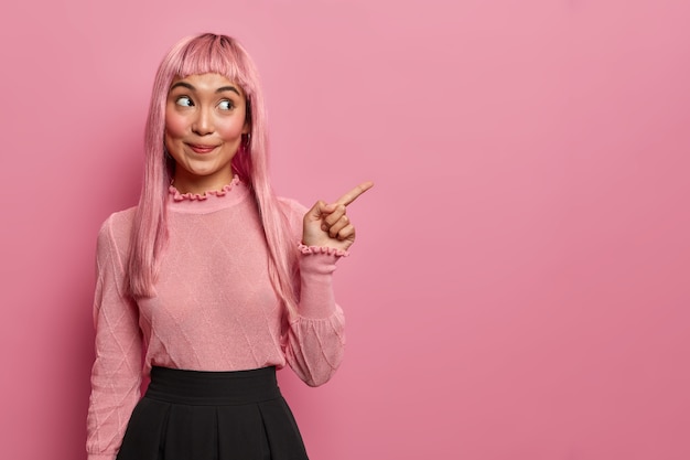 Mulher feliz e misteriosa do leste tem cabelo comprido, aponta o dedo para o espaço da cópia, mostra o lugar para o seu anúncio, promove o banner da empresa ou produto