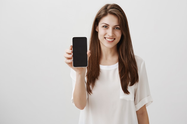 Mulher feliz e sorridente mostrando uma tela de celular, um aplicativo recomendado ou um site de compras