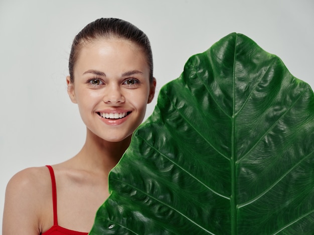 Mulher feliz em maiô vermelho rindo com a boca bem aberta e modelo de pele limpa de palmeira de folhas verdes