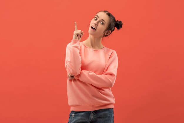 Mulher feliz em pé e sorrindo, isolado no fundo do estúdio coral. belo retrato feminino de meio corpo. jovem mulher emocional apontando para cima. as emoções humanas, o conceito de expressão facial.