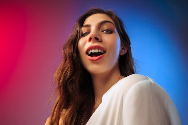 Mulher feliz em pé, sorrindo no fundo colorido do estúdio. Belo retrato feminino de meio corpo. Jovem satisfazer a mulher. Emoções humanas, conceito de expressão facial.