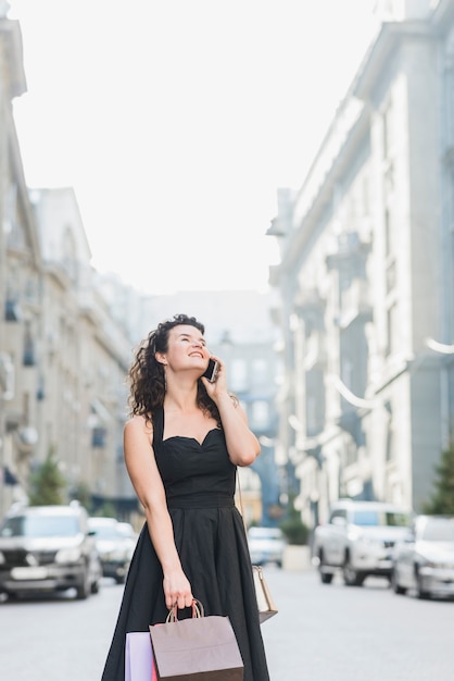 Foto grátis mulher feliz falando no celular enquanto carregava sacolas de compras