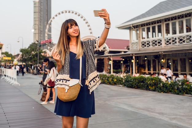 Foto grátis mulher feliz fazendo auto-retrato em fundo de roda gigante, caminhando na margem do rio.