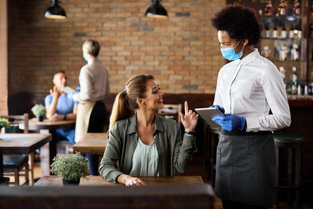 Mulher feliz fazendo um pedido enquanto conversa com garçonete negra em um café