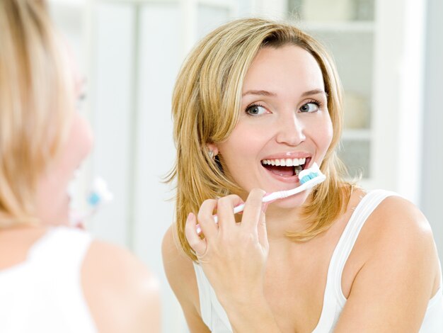 mulher feliz limpando os dentes com escova de dentes