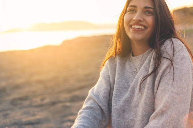 Mulher feliz na camisola sentado na costa do mar de areia