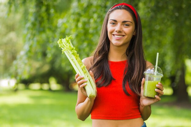 Mulher feliz no parque segurando aipo e smoothie