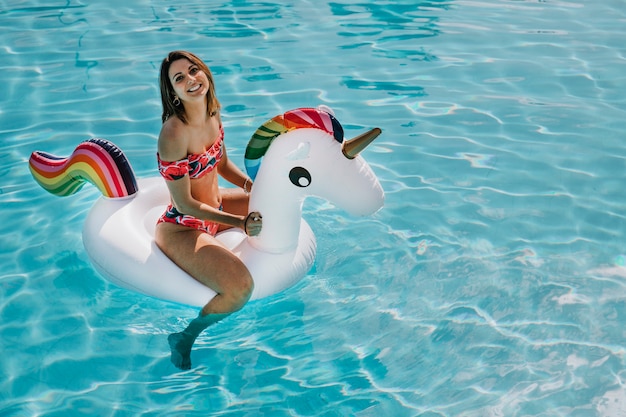 Mulher feliz no unicórnio inflável na piscina