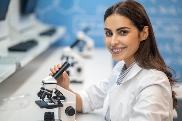 Foto grátis mulher feliz perto de microscópio olhando para a câmera
