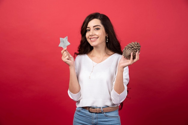 Mulher feliz posando com grande pinha de Natal e estrela sobre fundo vermelho. Foto de alta qualidade