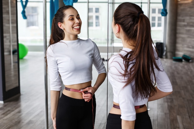 Foto grátis mulher feliz se olha no espelho segurando uma fita métrica na cintura