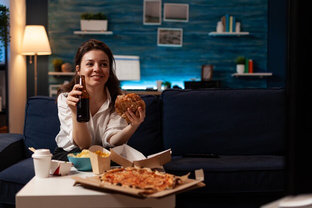 Mulher feliz segurando uma garrafa de cerveja e comendo comida saborosa para viagem