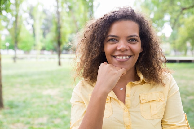 Mulher feliz tocando o queixo e posando para a câmera no parque da cidade