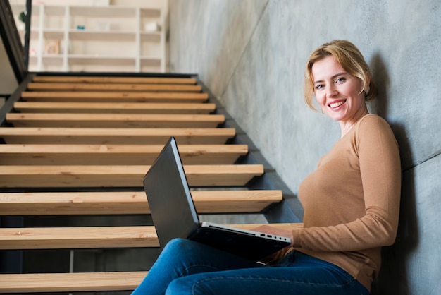Mulher feliz usando laptop nas escadas