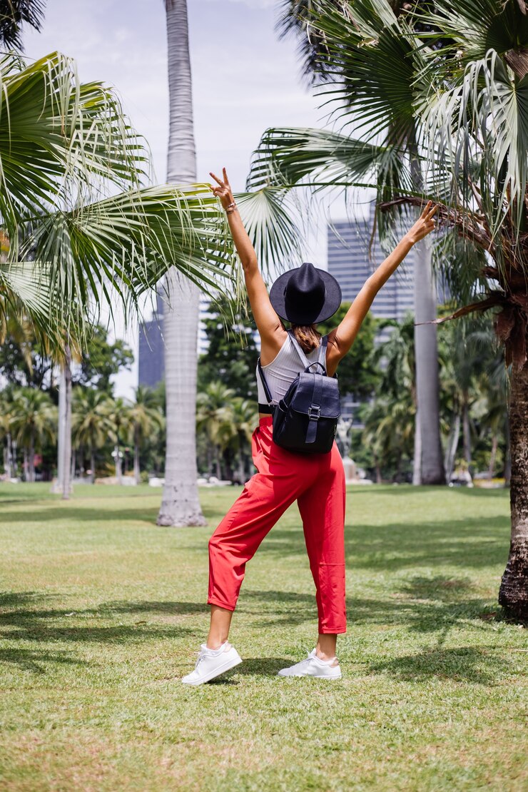 Foto grátis mulher feliz viajando por bangkok com uma mochila, aproveitando um lindo dia de sol no parque tropical em um campo de grama verde