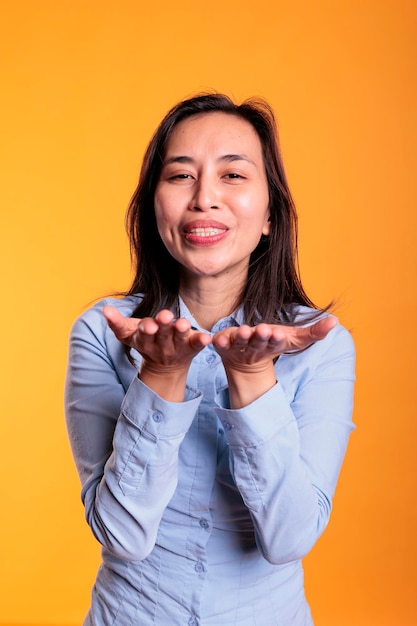 Mulher filipina morena alegre soprando ar beijada durante foto de estúdio, posando sobre fundo amarelo. jovem adulto positivo expressando amor, olhando para a câmera com um sorriso sedutor. gesto romântico