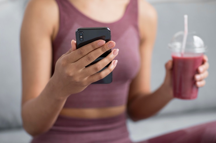 Foto grátis mulher fitness tomando um suco desintoxicante enquanto usa um smartphone