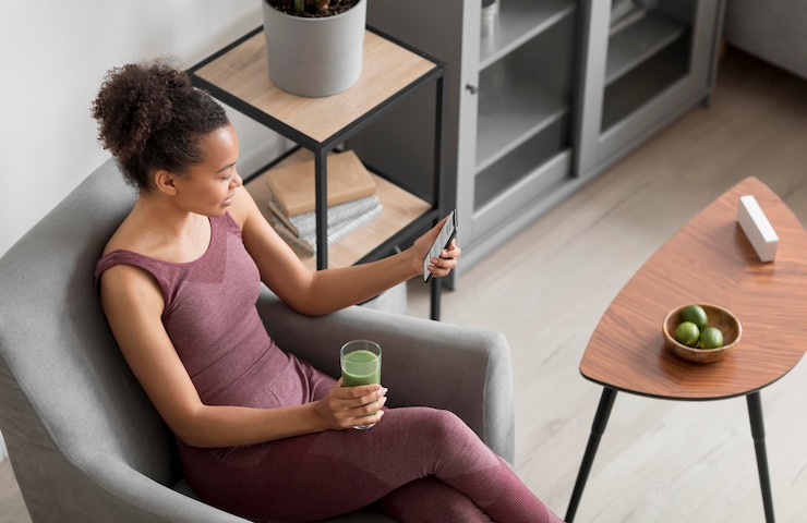 Foto grátis mulher fitness tomando um suco desintoxicante enquanto usa um smartphone