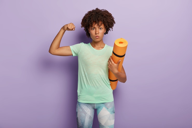 Foto grátis mulher forte e poderosa levanta o braço, mostra o bíceps, segura o colchonete para treino de ginástica, vestida com roupa ativa