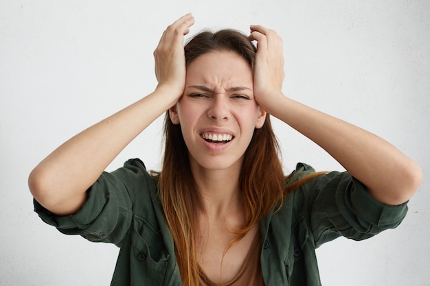 Foto grátis mulher frustrada tendo uma terrível dor de cabeça, mantendo as mãos na cabeça, franzindo a testa com dor, parecendo infeliz e estressante. dona de casa em desespero tendo situação estressante em sua vida sofrendo