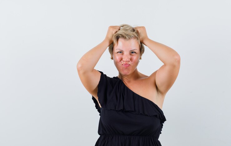 Foto grátis mulher glamorosa com blusa preta posando com as mãos na cabeça enquanto faz beicinho e parece autoconfiante
