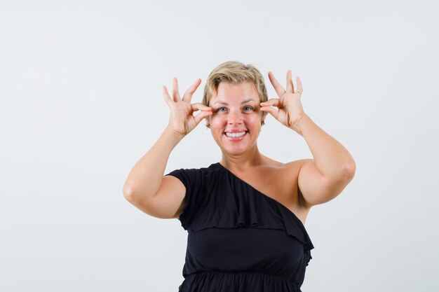 Mulher glamorosa mostrando gesto de ok em blusa preta e parecendo satisfeita