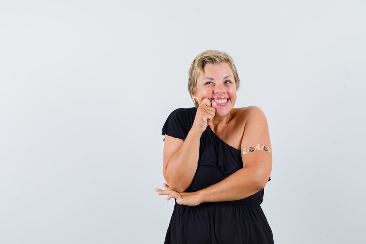 Foto grátis mulher glamourosa sorrindo enquanto segura a mão em sua bochecha com uma blusa preta e parecendo alegre