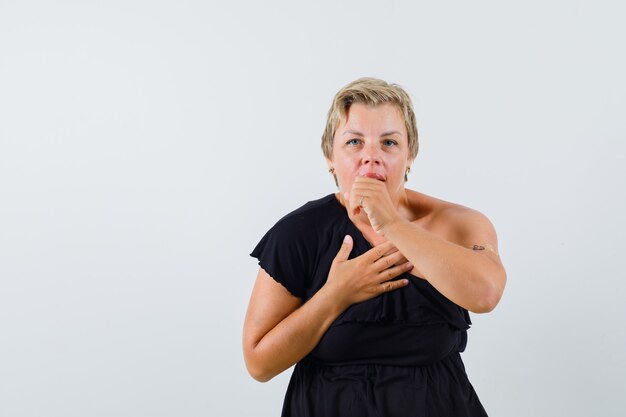 Mulher glamourosa tossindo em blusa preta e parecendo desconfortável