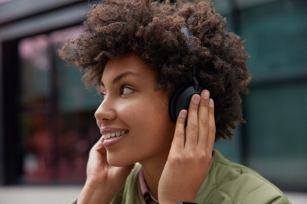mulher gosta de faixa de áudio em fones de ouvido sem fio usa aplicativo para ouvir músicas fica feliz se prepara para descanso de treinamento cardiovascular em ambiente urbano gosta de seu novo equipamento estéreo