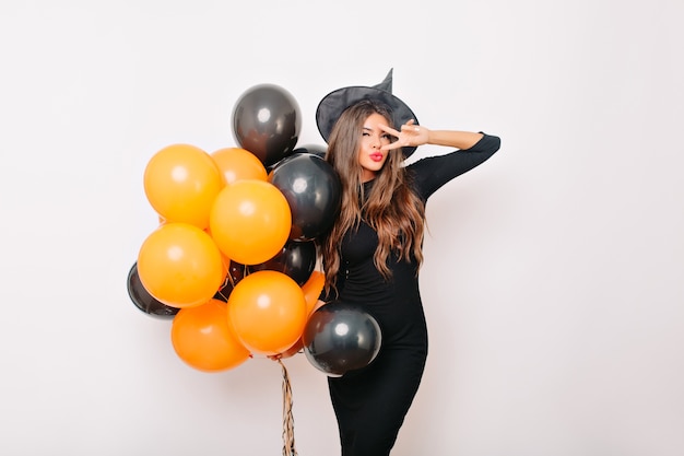 Mulher graciosa e charmosa com chapéu de bruxa segurando balões de hélio