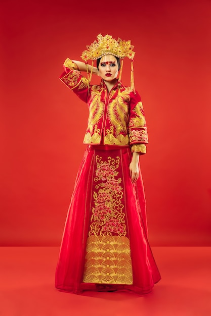 Mulher graciosa tradicional chinesa em estúdio sobre fundo vermelho. Linda garota vestindo traje nacional. Ano Novo Chinês, elegância, graça, artista, performance, dança, atriz, conceito de emoções