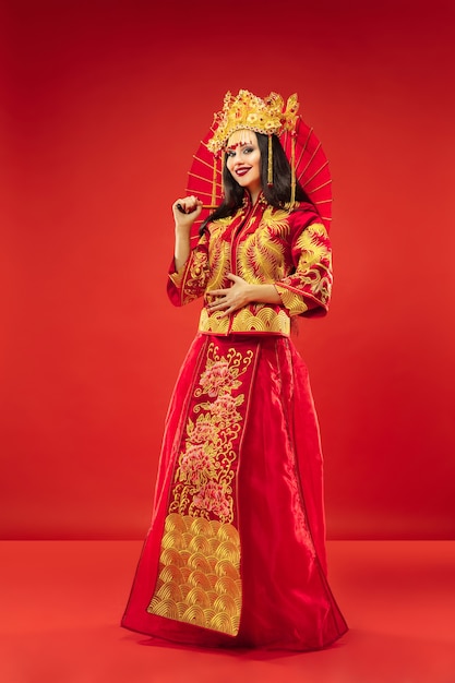 Mulher graciosa tradicional chinesa em estúdio sobre fundo vermelho. Linda garota vestindo traje nacional. Ano Novo Chinês, elegância, graça, artista, performance, dança, atriz, conceito de vestido