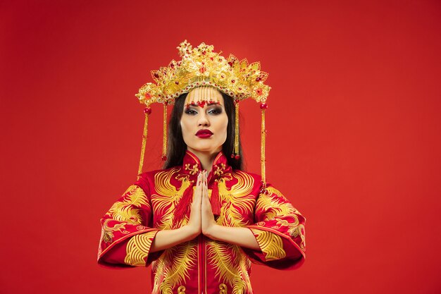 Mulher graciosa tradicional chinesa em estúdio sobre fundo vermelho. Linda garota vestindo traje nacional. Ano Novo Chinês, elegância, graça, artista, performance, dança, atriz, conceito de vestido