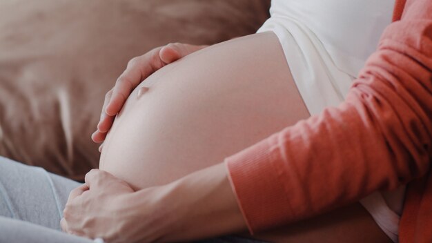 Mulher gravida asiática nova que guarda sua barriga que fala com sua criança. Mãe, sentindo-se feliz sorrindo positivo e tranquilo enquanto cuida bebê, gravidez, deitado no sofá na sala de estar em casa.