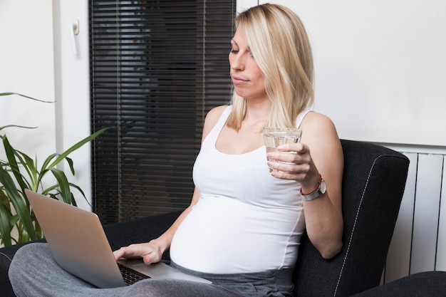 Mulher grávida com laptop e copo de água