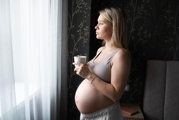 Mulher grávida com tiro médio segurando o copo