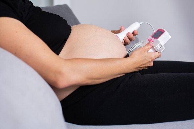 Mulher grávida com um doppler fetal ouvindo o coração do bebê sentado