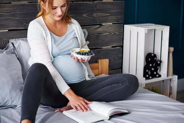 Mulher grávida comendo e lendo um livro