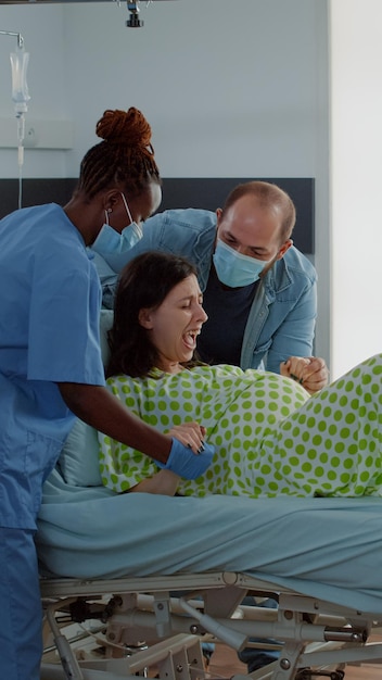 Foto grátis mulher grávida dando à luz na cama da enfermaria de hospital com o médico obstetra e a enfermeira afro-americana, dando suporte e assistência médica. jovem sentado com a esposa para o parto