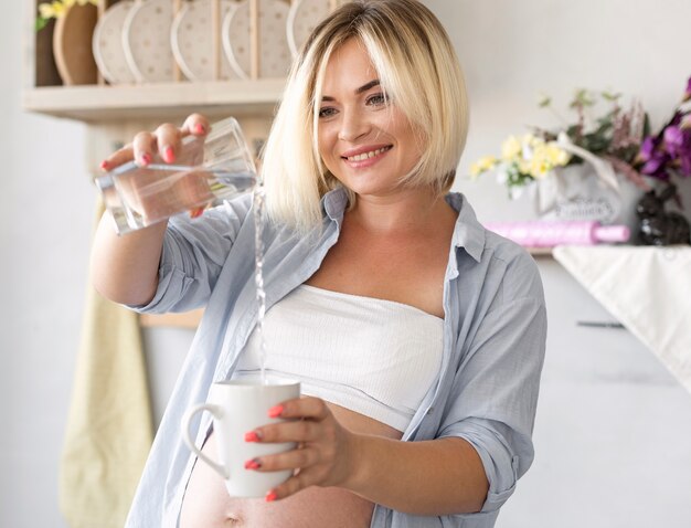 Mulher grávida derramando água em um copo