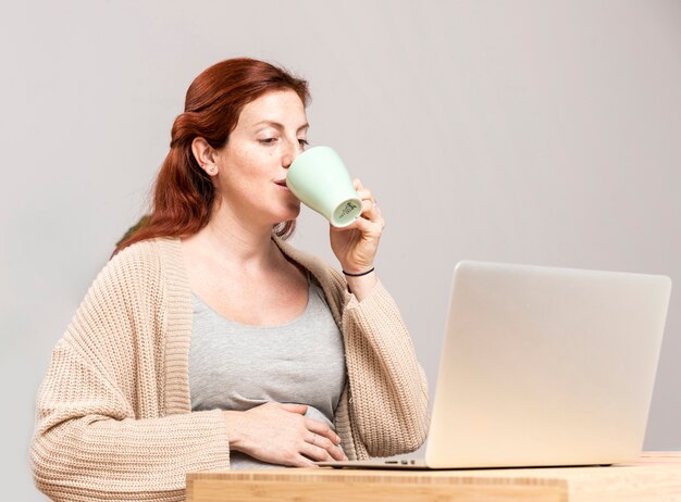 Mulher grávida em casa bebendo chá enquanto estiver usando o laptop