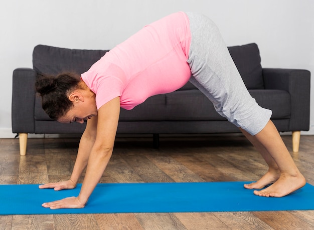 Foto grátis mulher grávida em casa com esteira para exercícios praticando posição de ioga