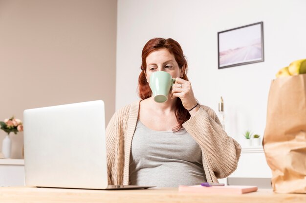 Mulher gravida em casa olhando no laptop
