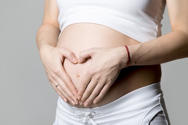 Mulher gravida que faz um coração com as mãos