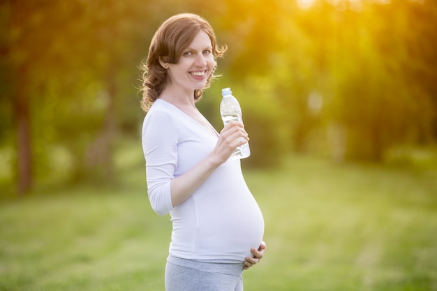 Mulher gravida que prende uma garrafa de água