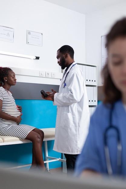 Mulher grávida recebendo um frasco de comprimidos para tratar o enjoo de um médico durante a visita de check-up. paciente grávida esperando filho, conversando com o médico sobre o tratamento por prescrição.