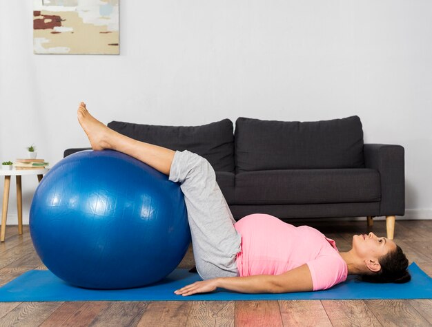 Mulher grávida se exercitando em casa no chão com bola